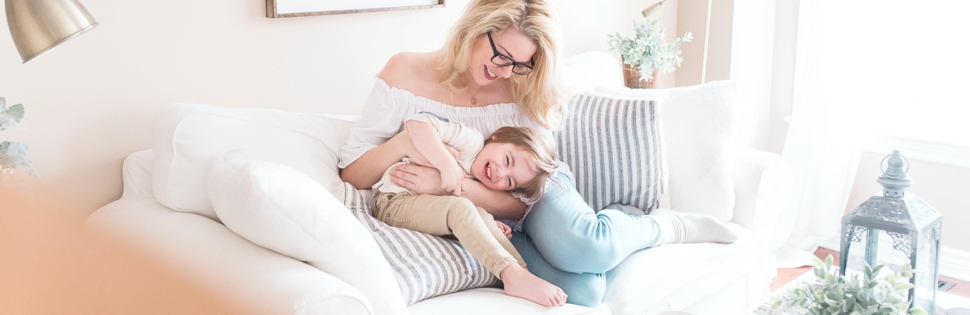 mum with glasses plays with her young boy on couch