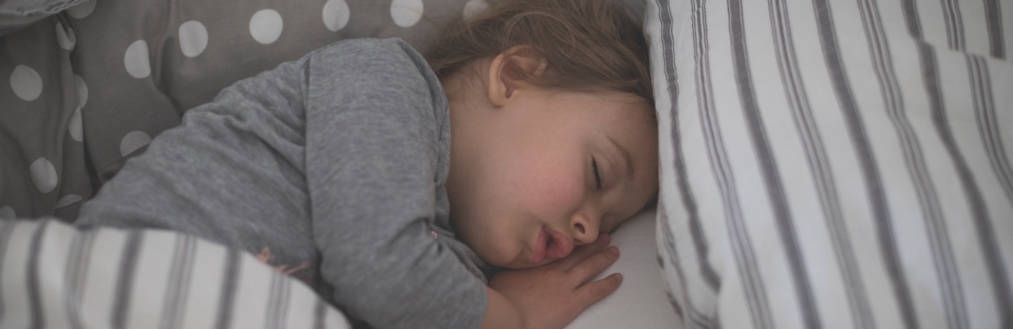 toddler with grey pyjamas sleeps on bed