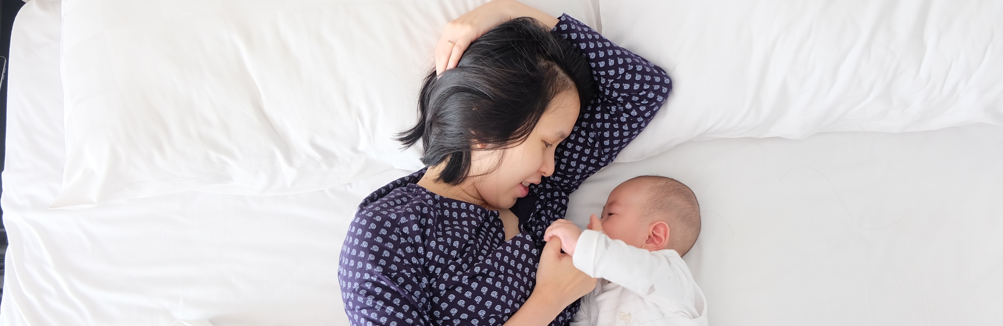 mother interacting with her baby on a white bed