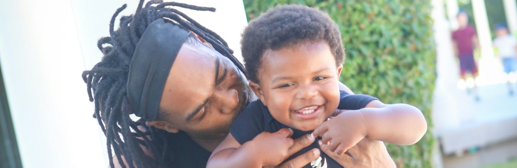 father with dreadlocks tickles giggling son