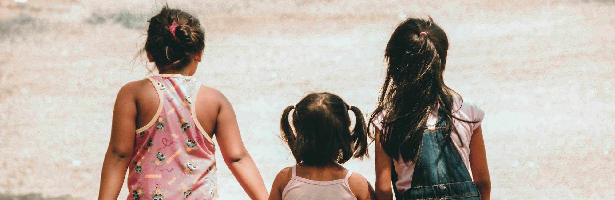 two young brown skinned girls walk with their younger sister