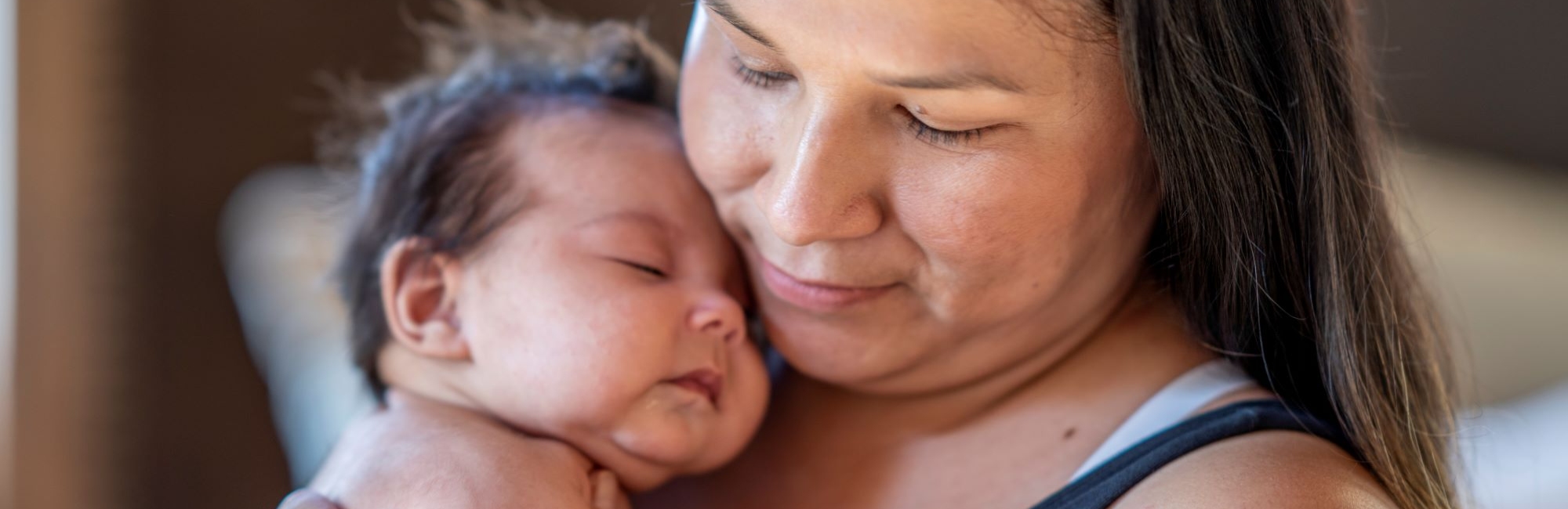 aboriginal mother holding her sleeping baby on chest and shoulder