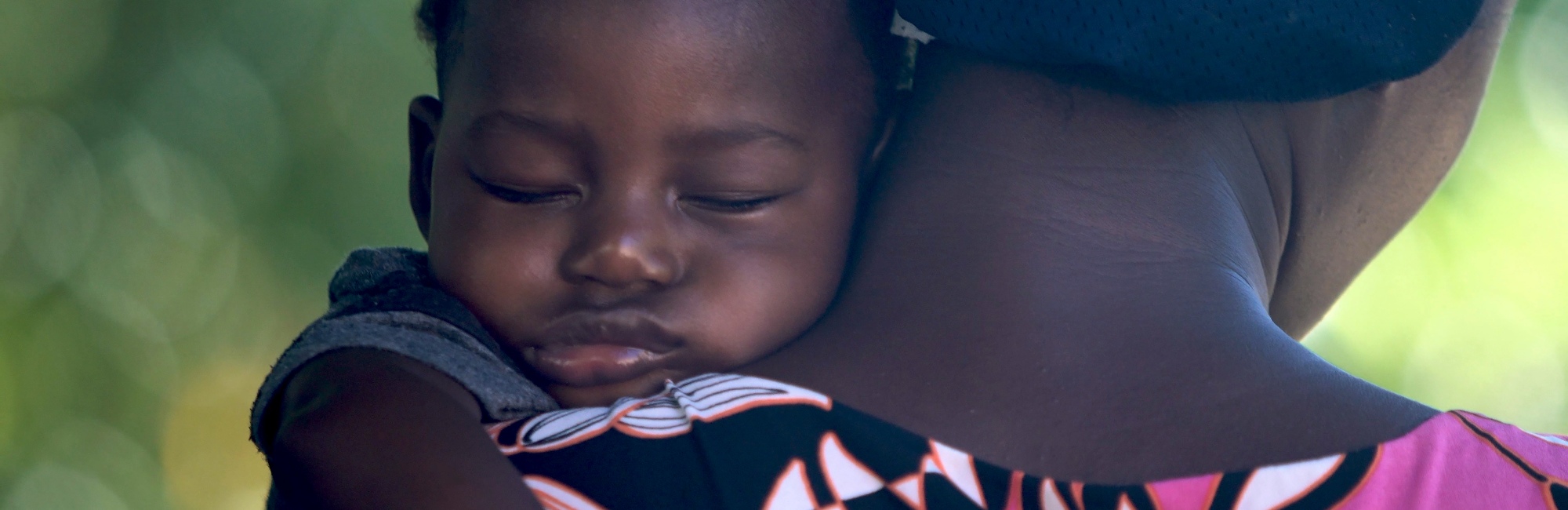 woman holds up her sleeping baby over her shoulder