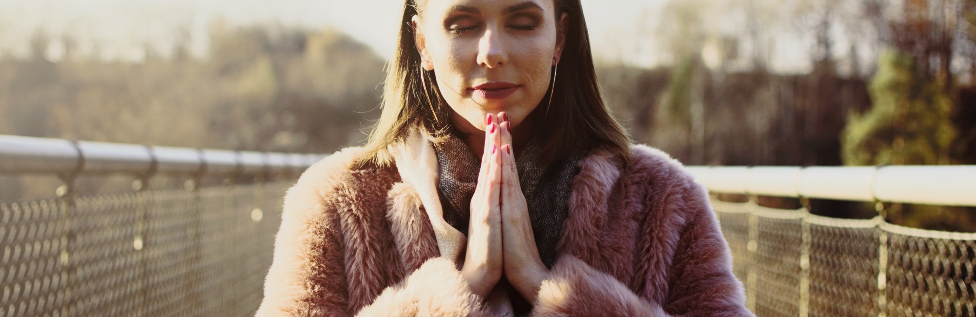 woman on bridge in pink coat with hands in prayer position