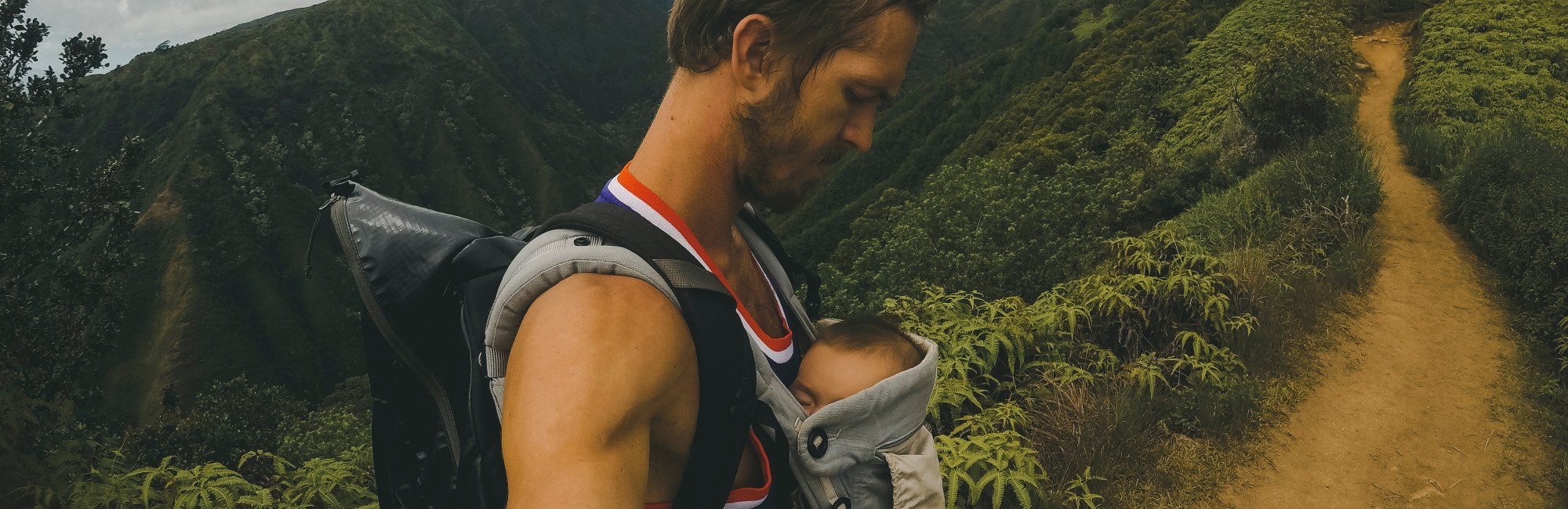 father uses baby carrier while hiking on mountain path