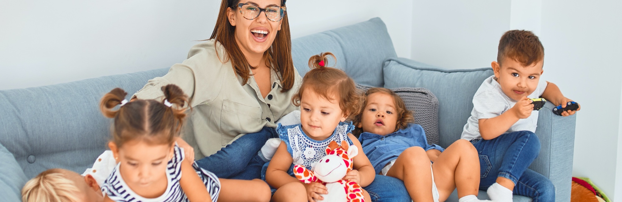 carer plays with lots of children on a sofa in childcare